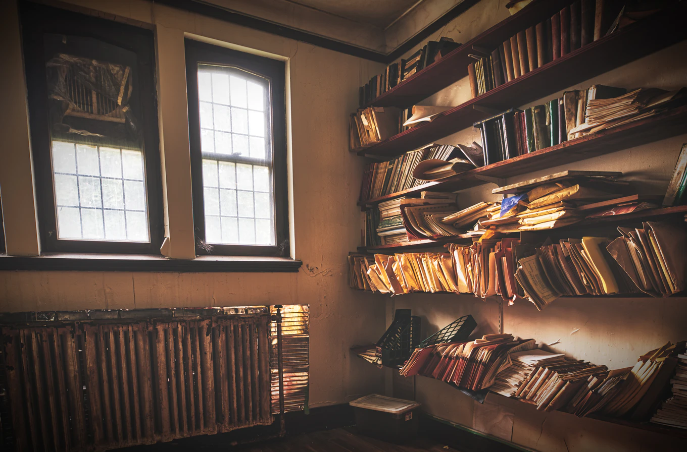 Picture of a dimly lit room with a disorganized array of books that are haphazardly stored on shelves.