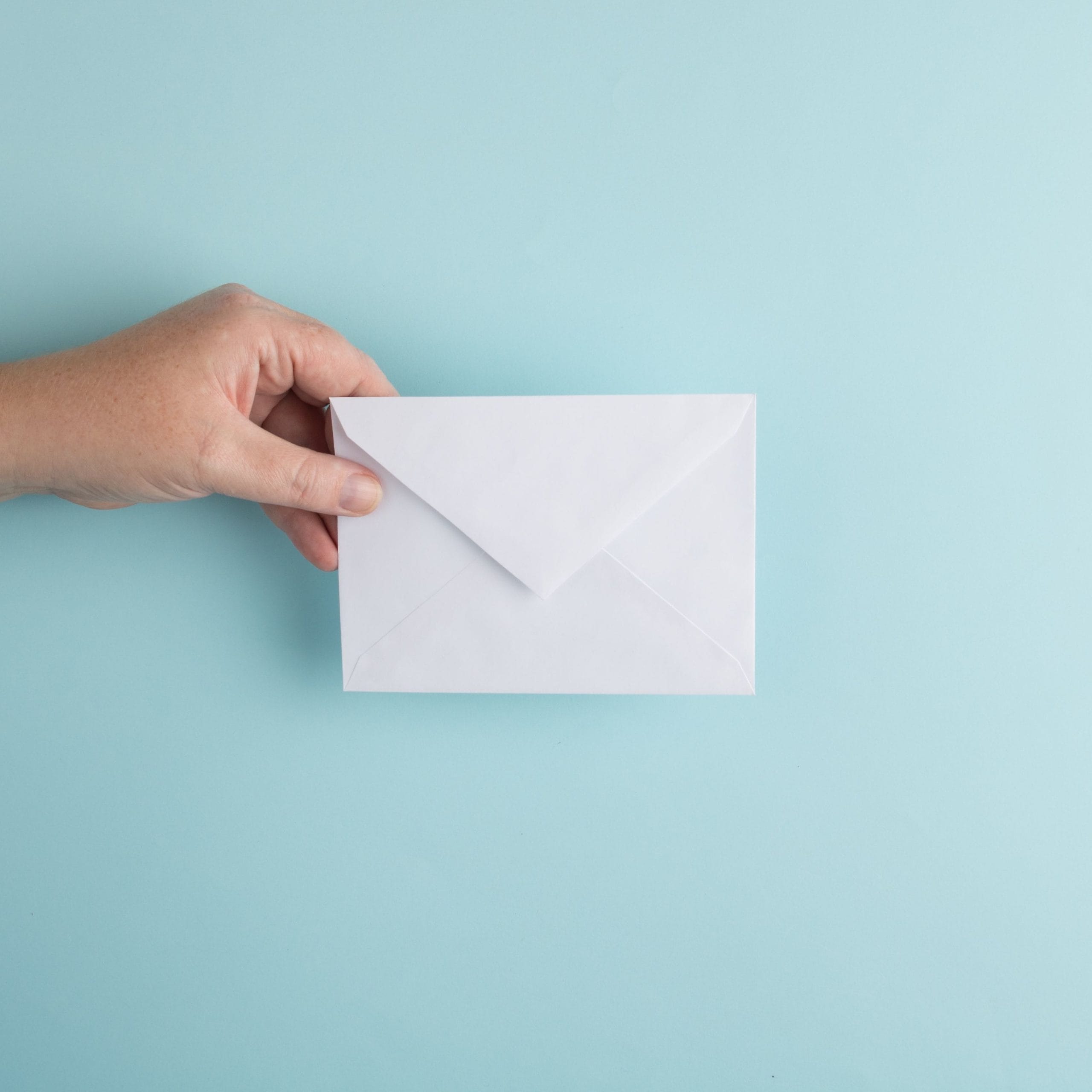 Plain white envelope being held up against a light blue background.