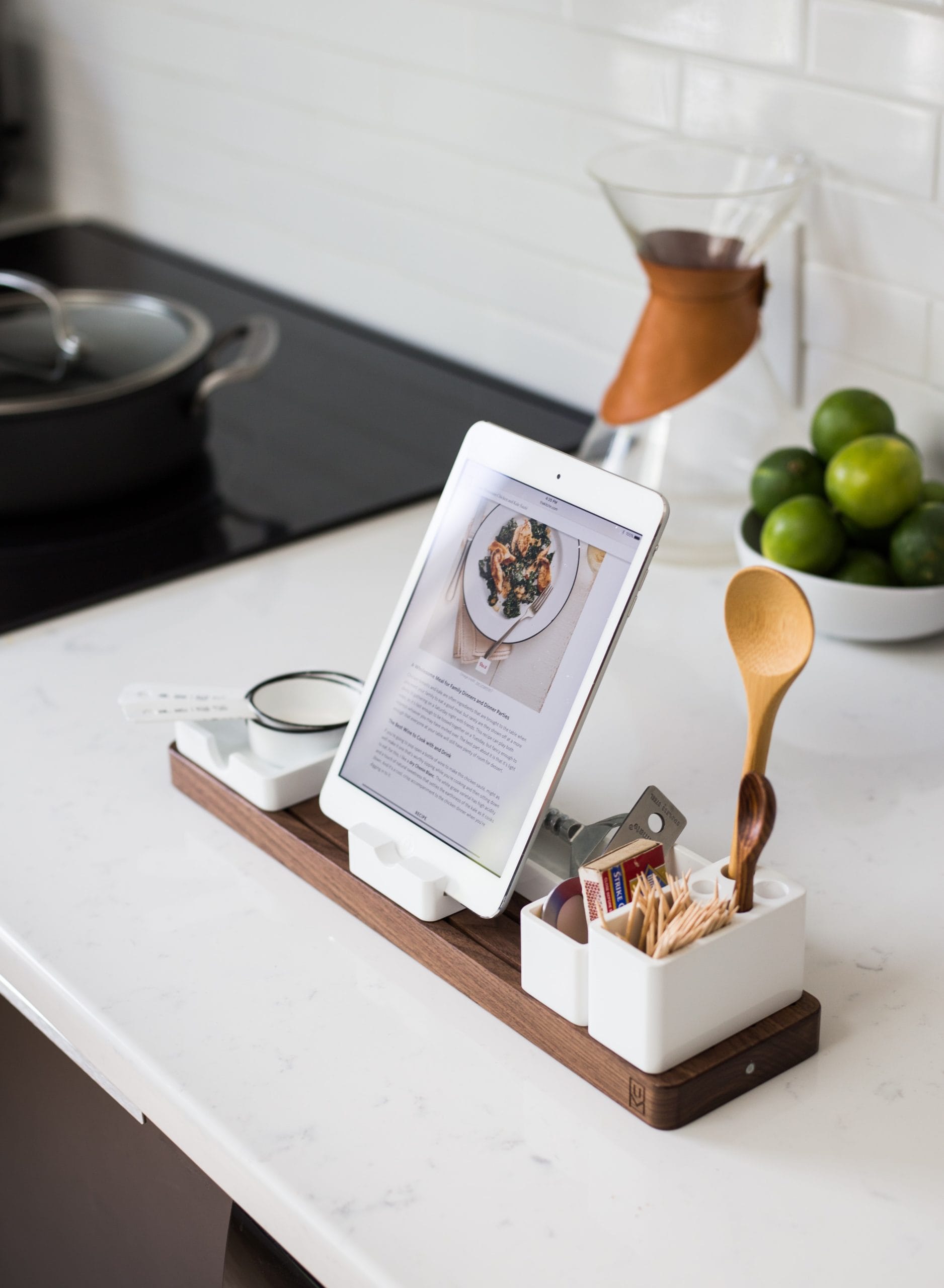 A tablet displaying a plate of food. The tablet is propped up on a kitchen table surrounded by various kitchen utensils.