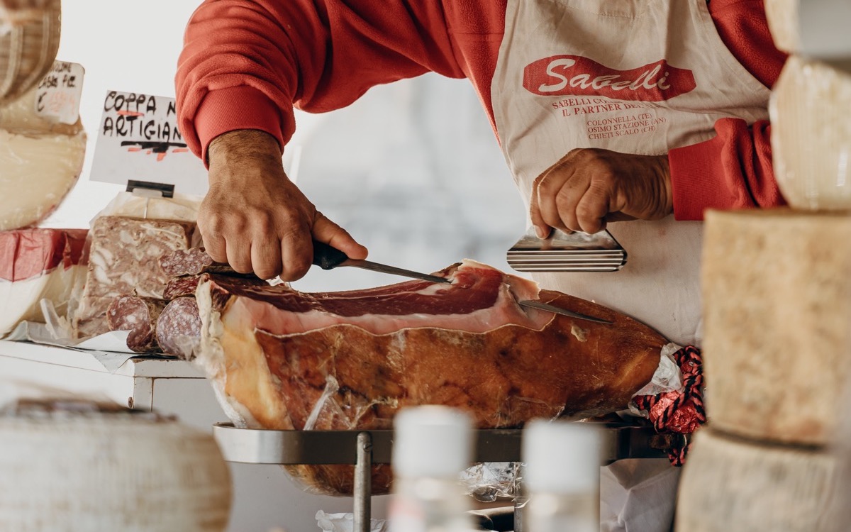 Closeup of a butcher carving into a big chunk of meat.