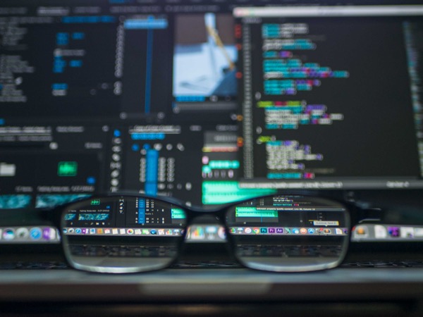 Close up picture of glasses frames in front of a computer screen displaying lines of code.