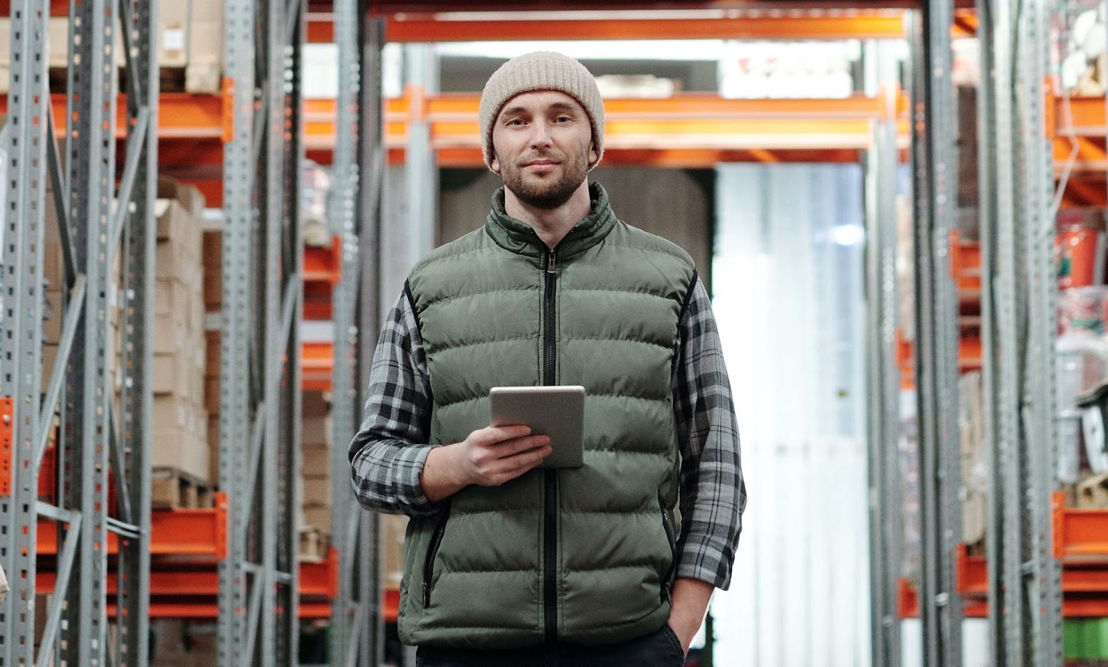 A confident worker thinks about automation in grocery stores, holding a tablet computer and dressed appropriately for a walk-in freezer, stands in their supermarket's commissary warehouse, ready to guide a direct store delivery back to the distribution center.