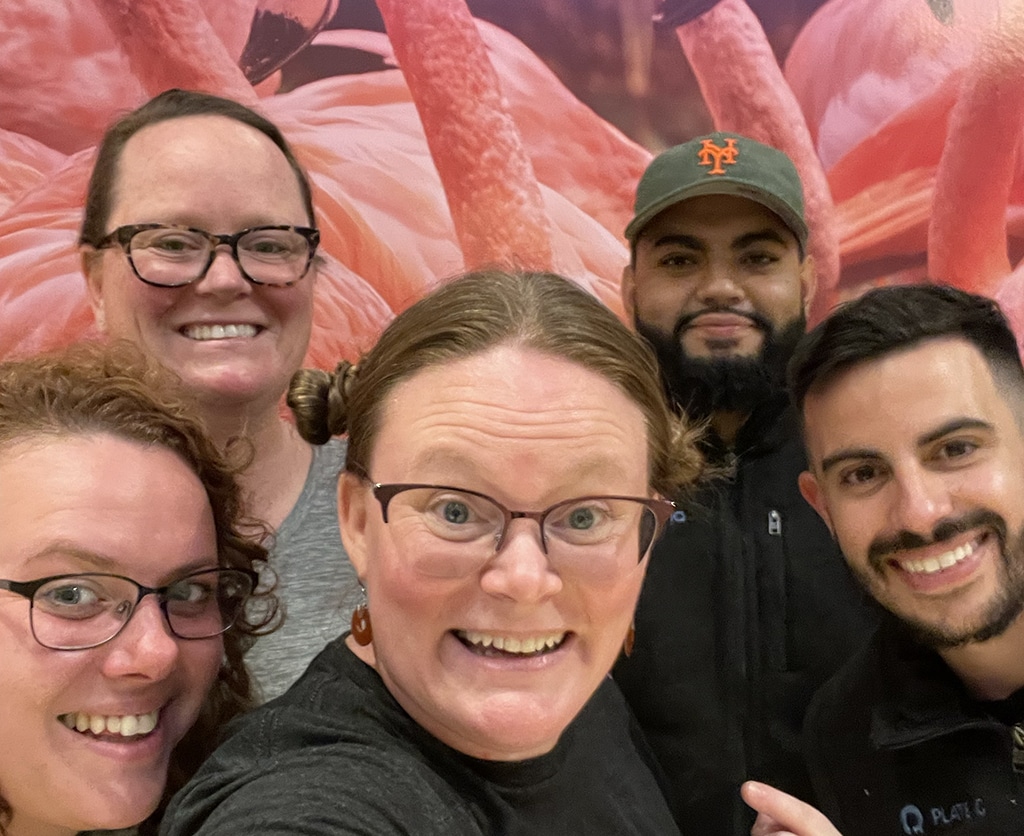 After-hours team selfie in front of a giant photo of flamingos. Happy Ottimate employees looking forward to dinner and rest before the next conference day.