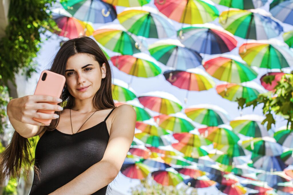 Picture of a person taking a selfie in front of many colorful hanging umbrellas.
