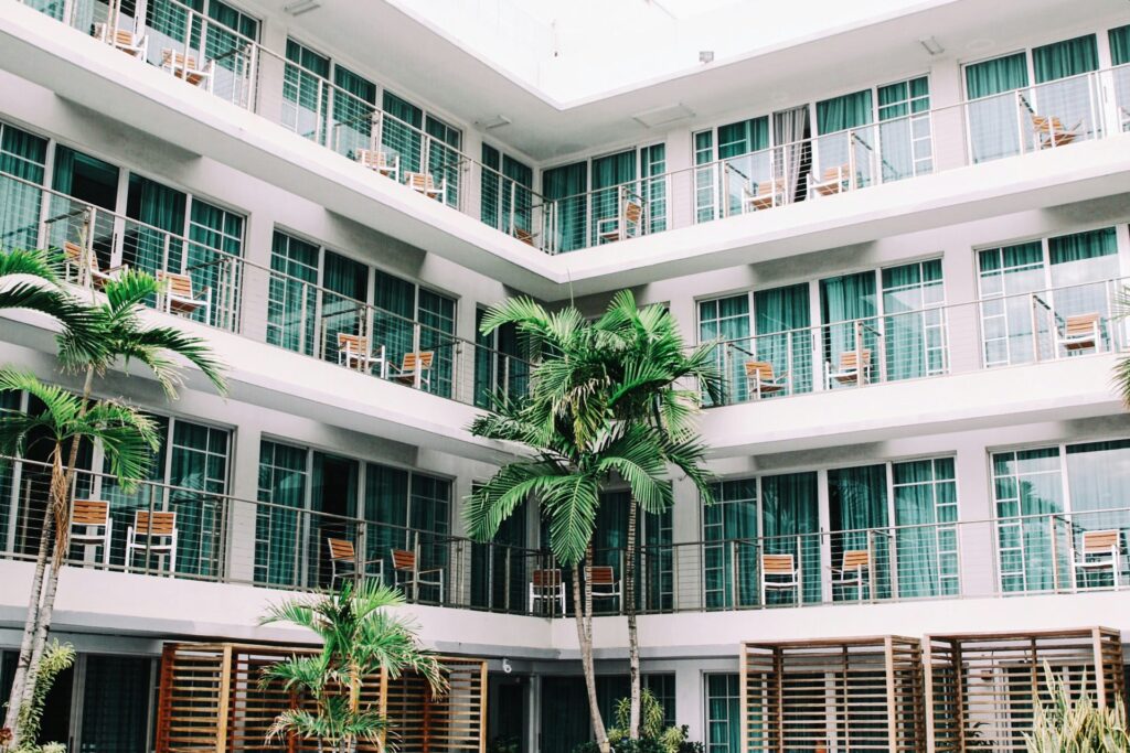 Picture of the exterior of a white hotel building with multiple balconies and palm trees.