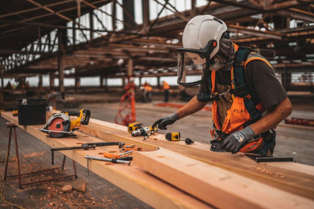 A construction worker drilling into a wooden plank outside of a construction site.