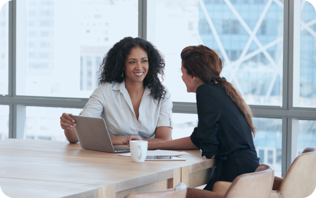 two business women sitting at a conference table in front of large windows