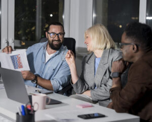 Three coworkers are in an office setting, looking at a graph.